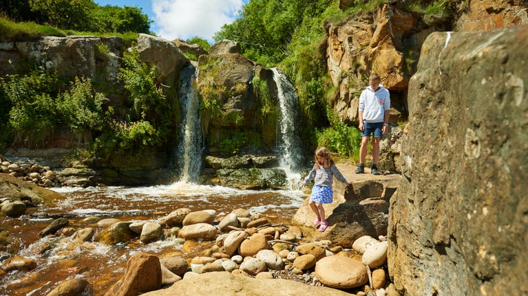 A boy and a girl making their way down the rocks to bottom of small waterfall